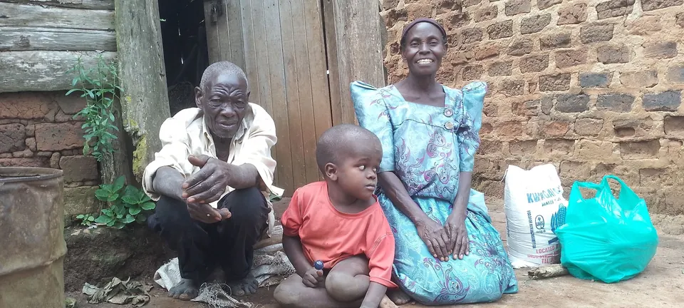 Familie mit einem Lebensmittelpaket vor ihrem Zuhause in Mukono